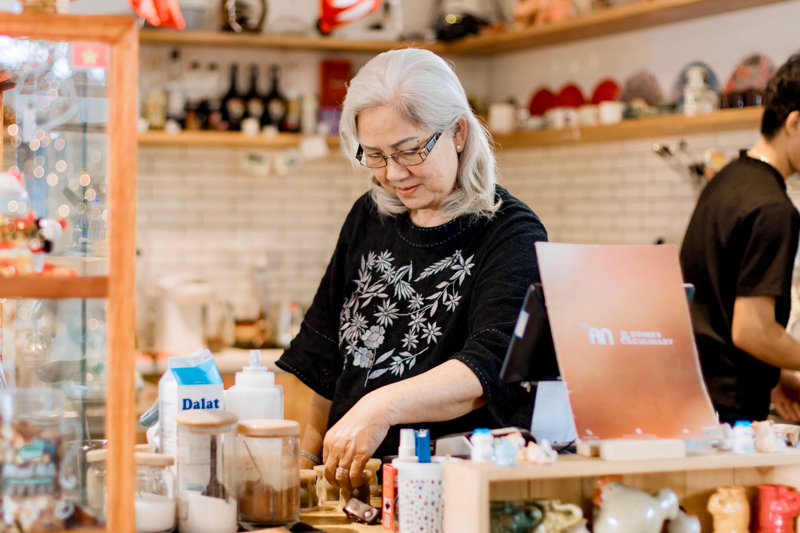 Dueña de una pequeña tienda-café, tranquila tras su mostrador, mientras Quibo se encarga de su presencia digital
